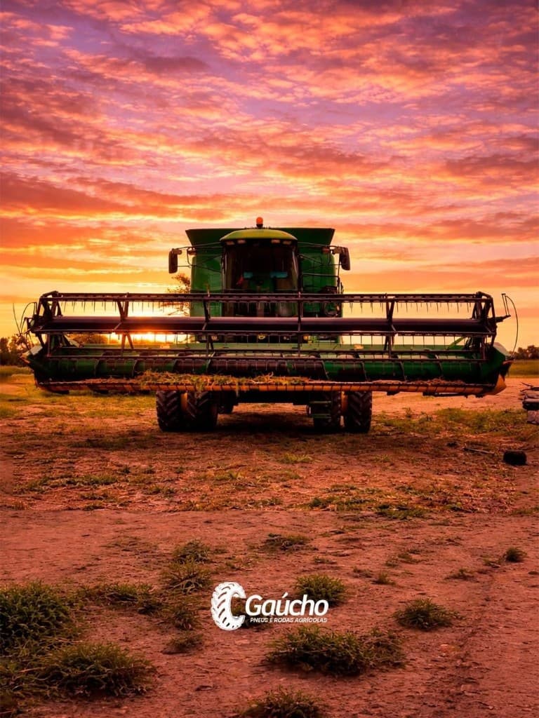 Colheitadeira verde de frente ao pôr do sol; arte promocional Gaúcho Pneus e Rodas Agrícolas.