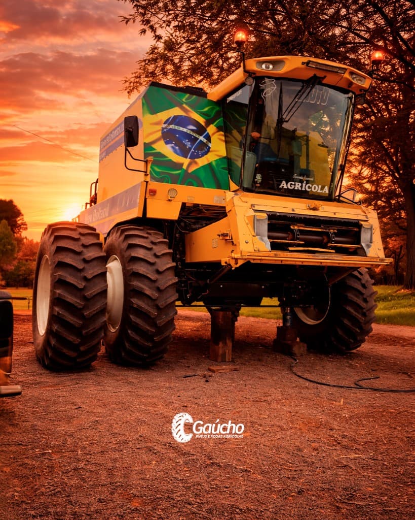 Colheitadeira amarela ao pôr do sol com bandeira brasileira; pneus e máquinas agrícolas — Gaúcho Pneus.