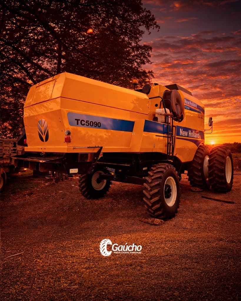 Colheitadeira New Holland em cascalho ao entardecer; cores quentes do pôr do sol — Gaúcho Pneus.